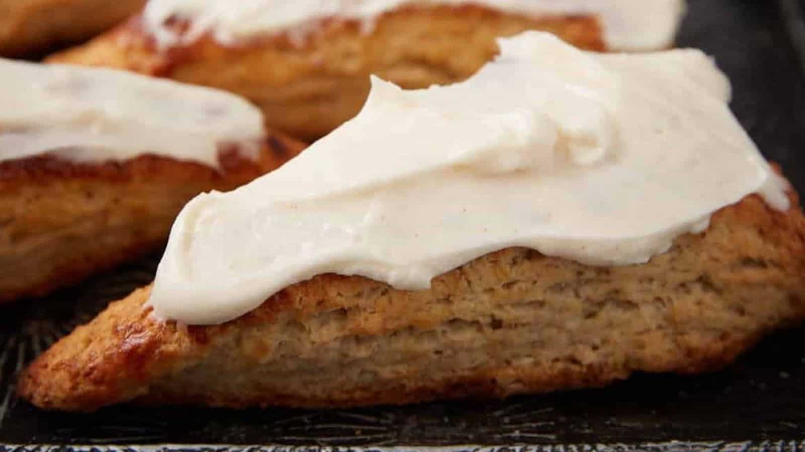 A triangular scone topped with a thick layer of white icing, resting on a dark surface.