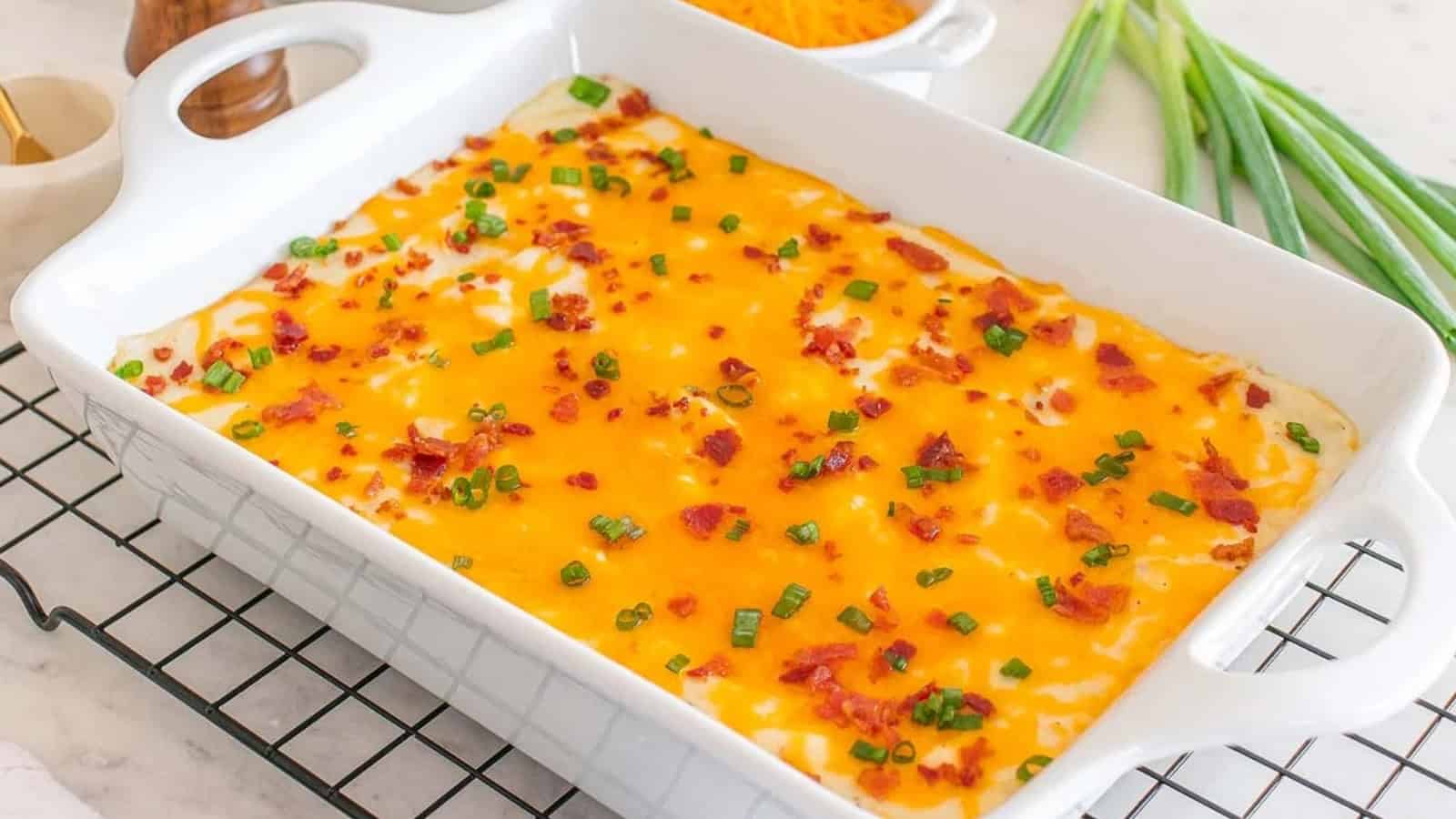 Casserole topped with melted cheese, bacon bits, and chopped green onions in a white baking dish.