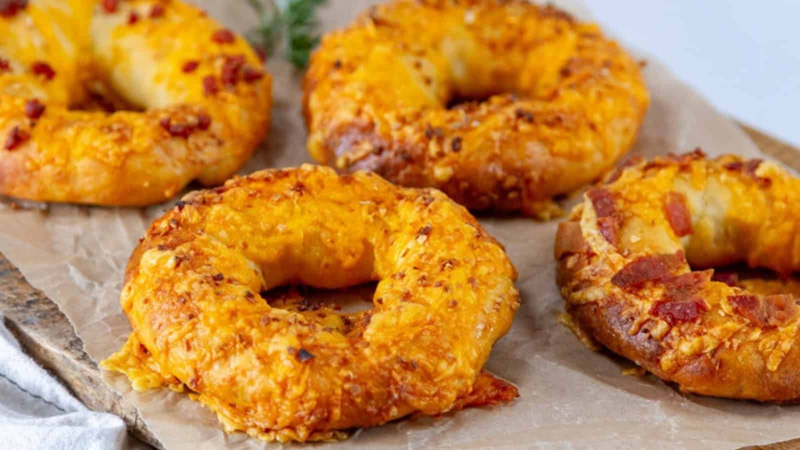 Four cheesy bagels with bits of bacon on parchment paper.