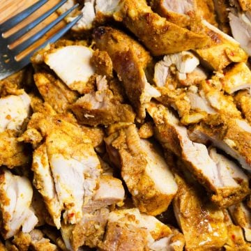 Slices of seasoned, cooked chicken with a fork visible in the corner.