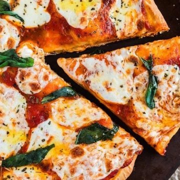A Margherita pizza with melted cheese and basil, with one slice being lifted on a spatula.