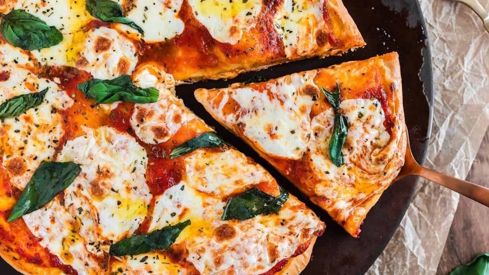 A Margherita pizza with melted cheese and basil, with one slice being lifted on a spatula.