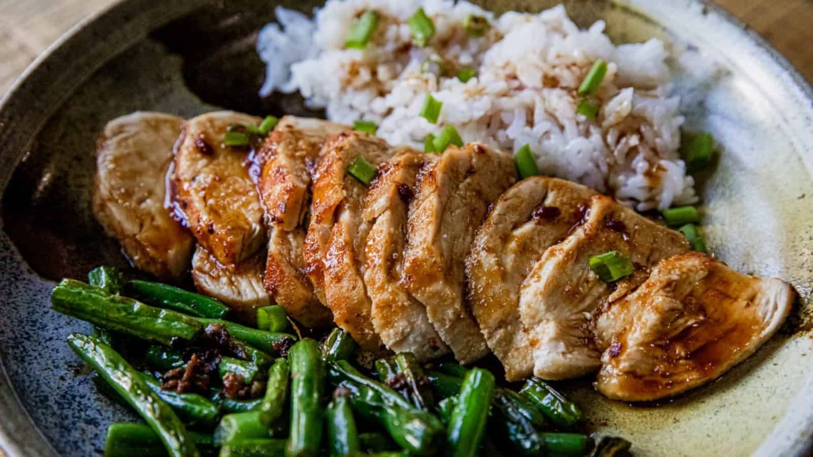 Sliced grilled chicken with green beans and white rice, garnished with chopped green onions on a plate.