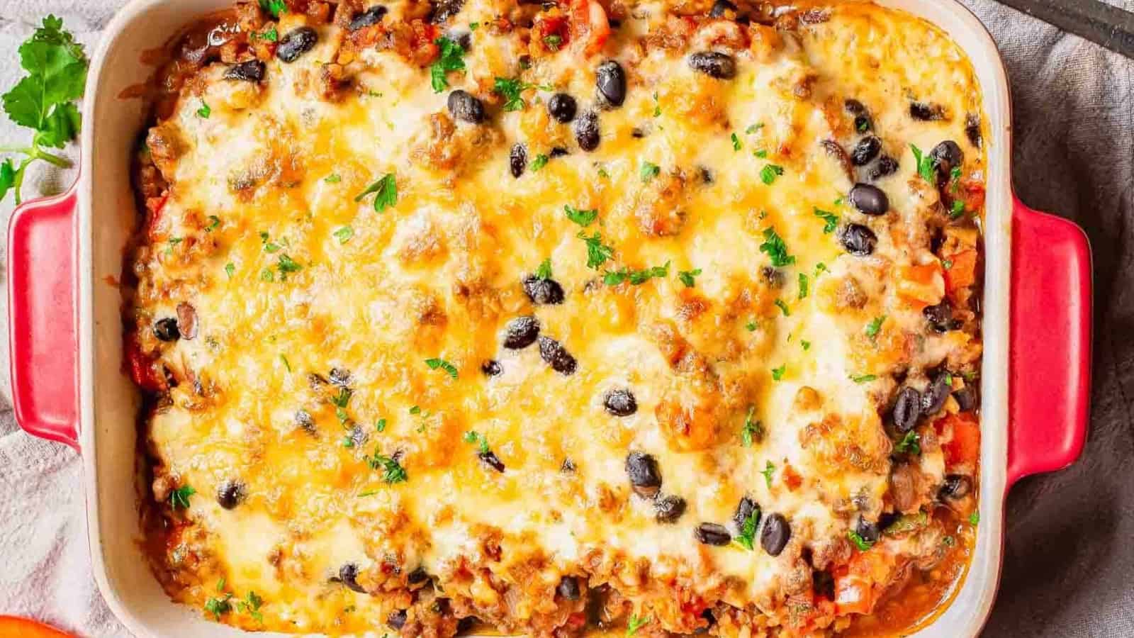 A cheesy baked casserole topped with black beans and parsley in a red baking dish.