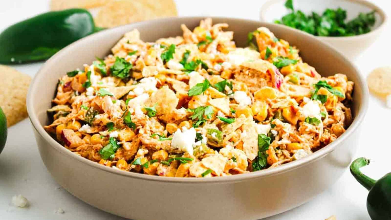 A bowl of chicken salad topped with crumbled cheese and fresh chopped parsley on a white table.