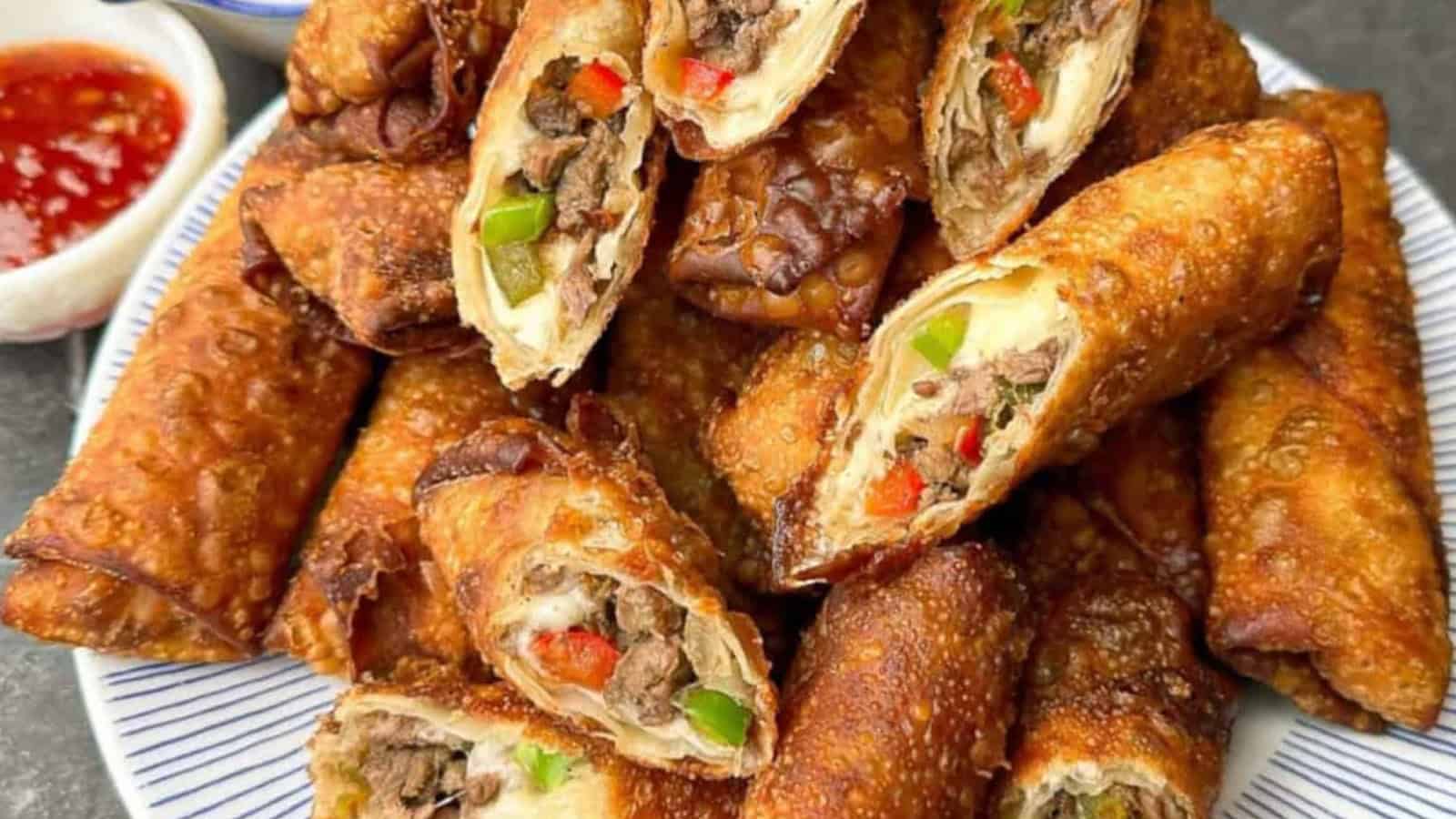 A plate of crispy egg rolls filled with beef, green and red peppers. A small dish of dipping sauce is visible on the side.