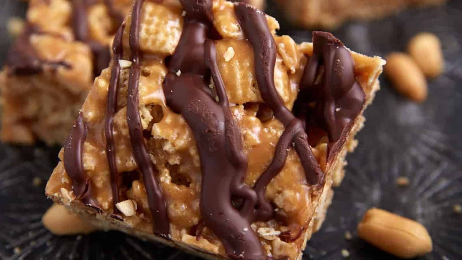 A peanut butter cereal bar drizzled with chocolate, with whole peanuts scattered nearby.