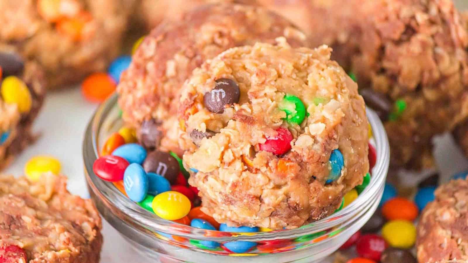 A glass bowl filled with cookies and colorful candy-coated chocolates, with more cookies in the background.