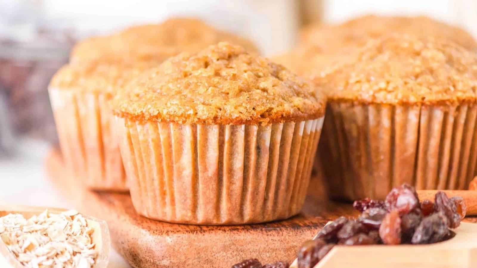 Bran muffins on a wooden board with oats and raisins in the foreground.