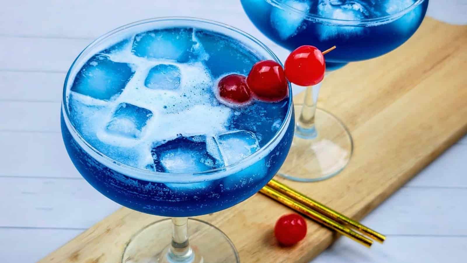 Two blue ocean water cocktails garnished with cherries.
