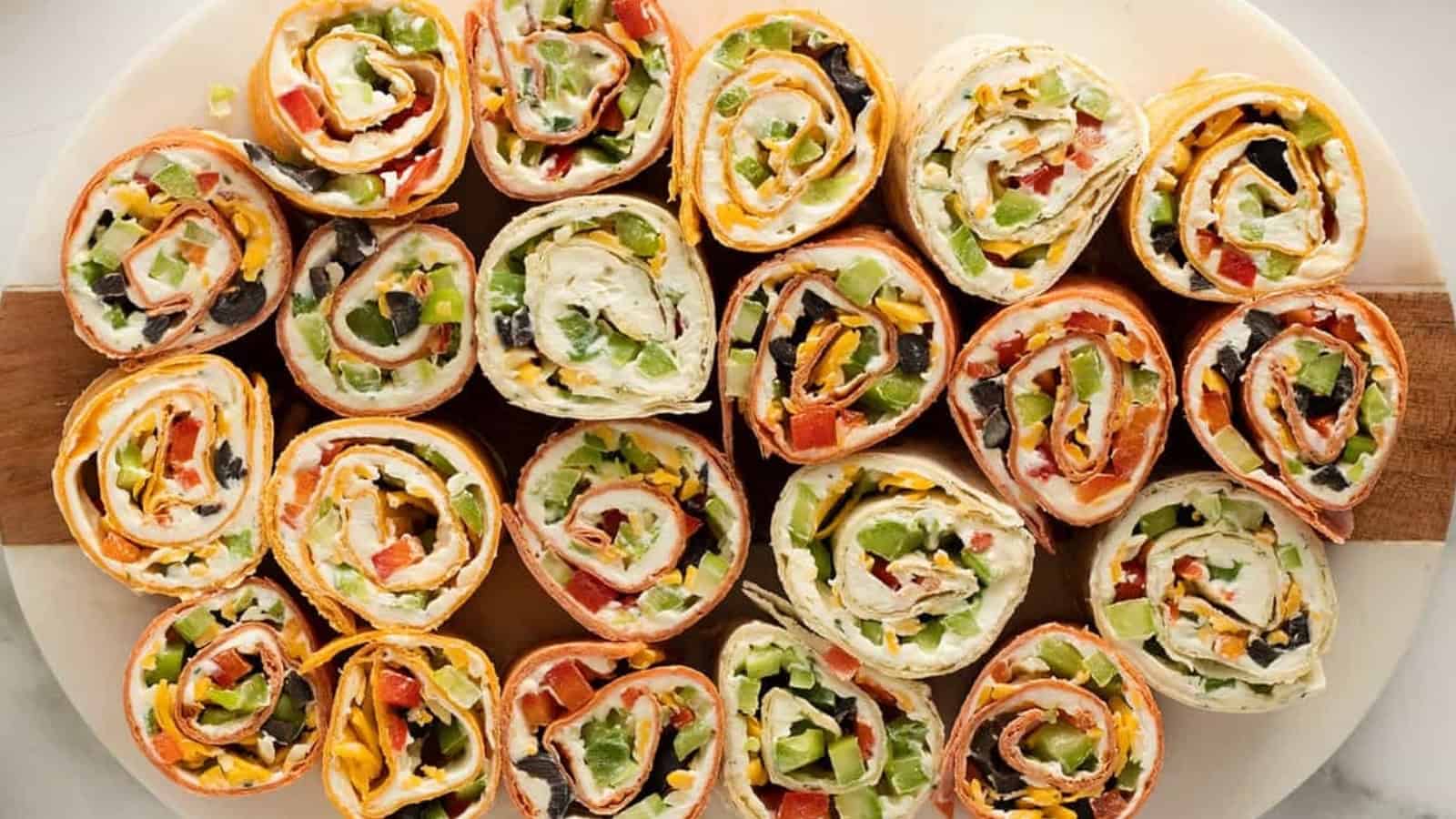 Colorful tortilla pinwheel sandwiches filled with cheese, veggies, and cream cheese, arranged on a platter.