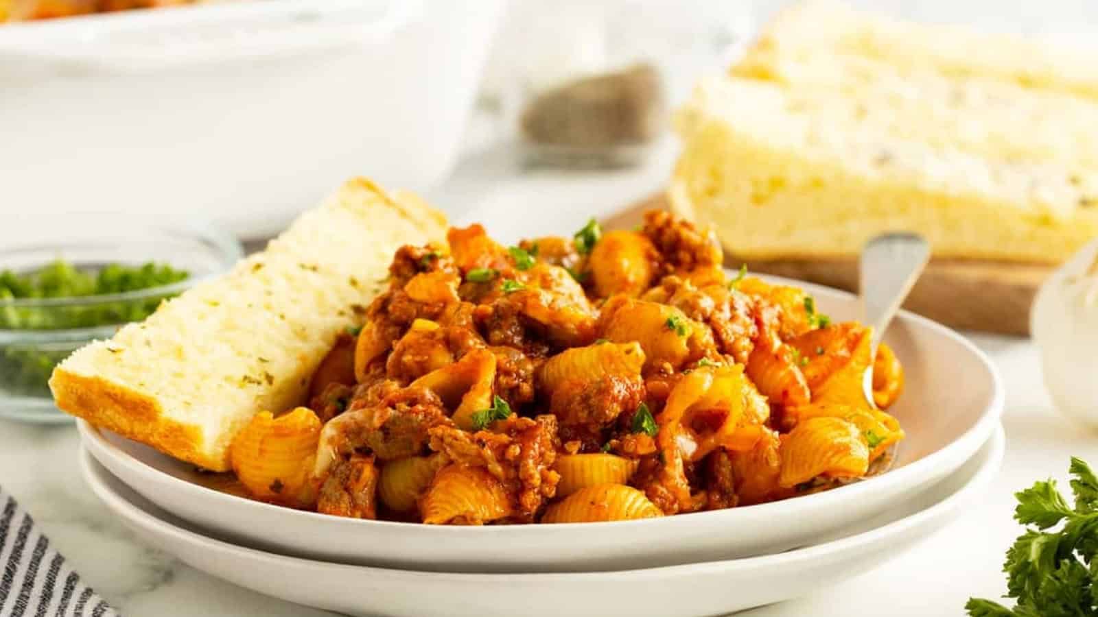 Pasta shells with meat sauce and herbs, served with garlic bread on a white plate.