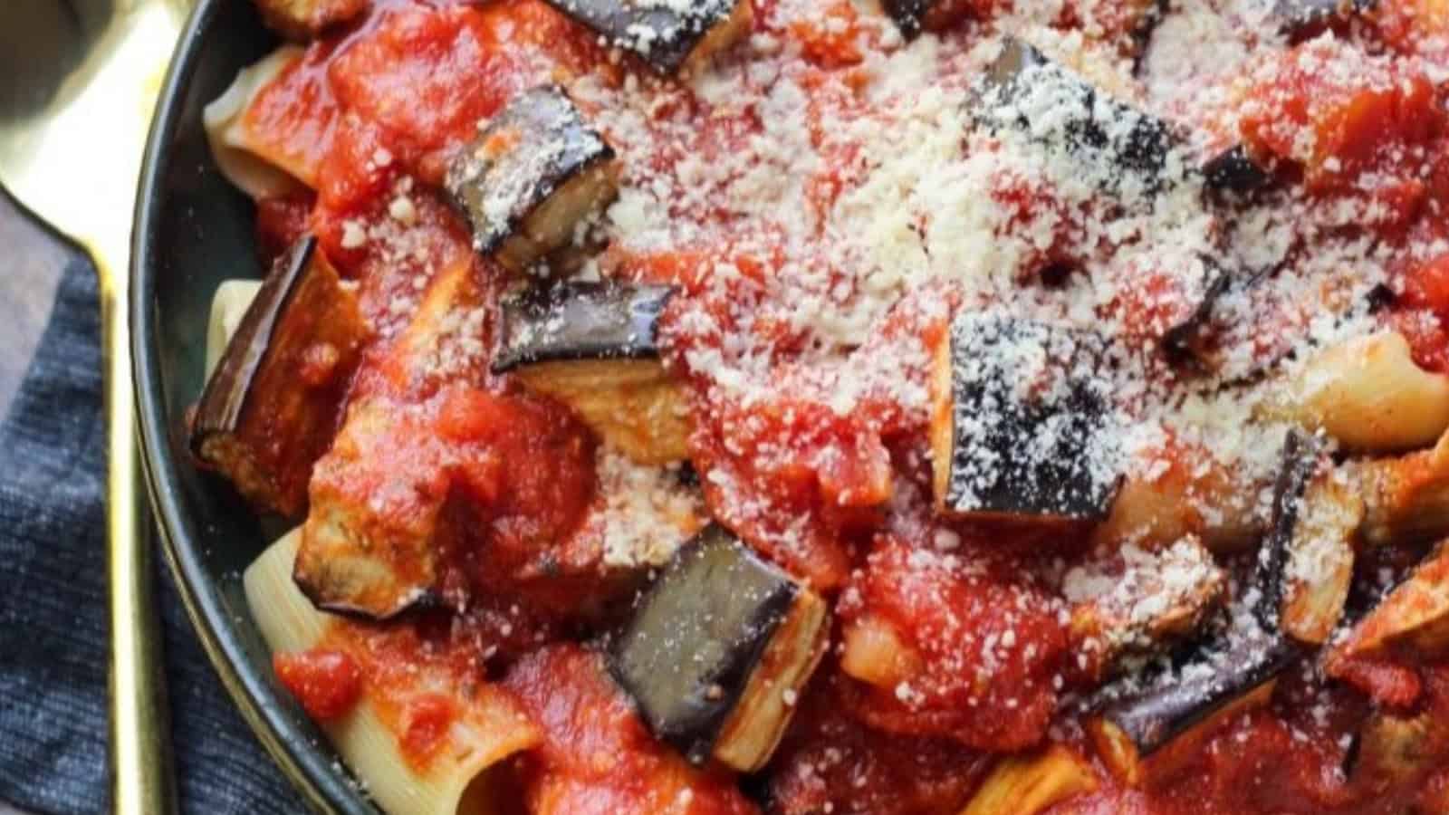 Pasta topped with tomato sauce, roasted eggplant, and grated cheese on a dark plate.