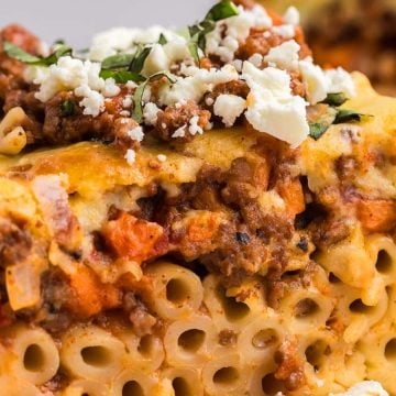 A close-up of a slice of baked pasta with meat sauce, topped with cheese and fresh herbs.