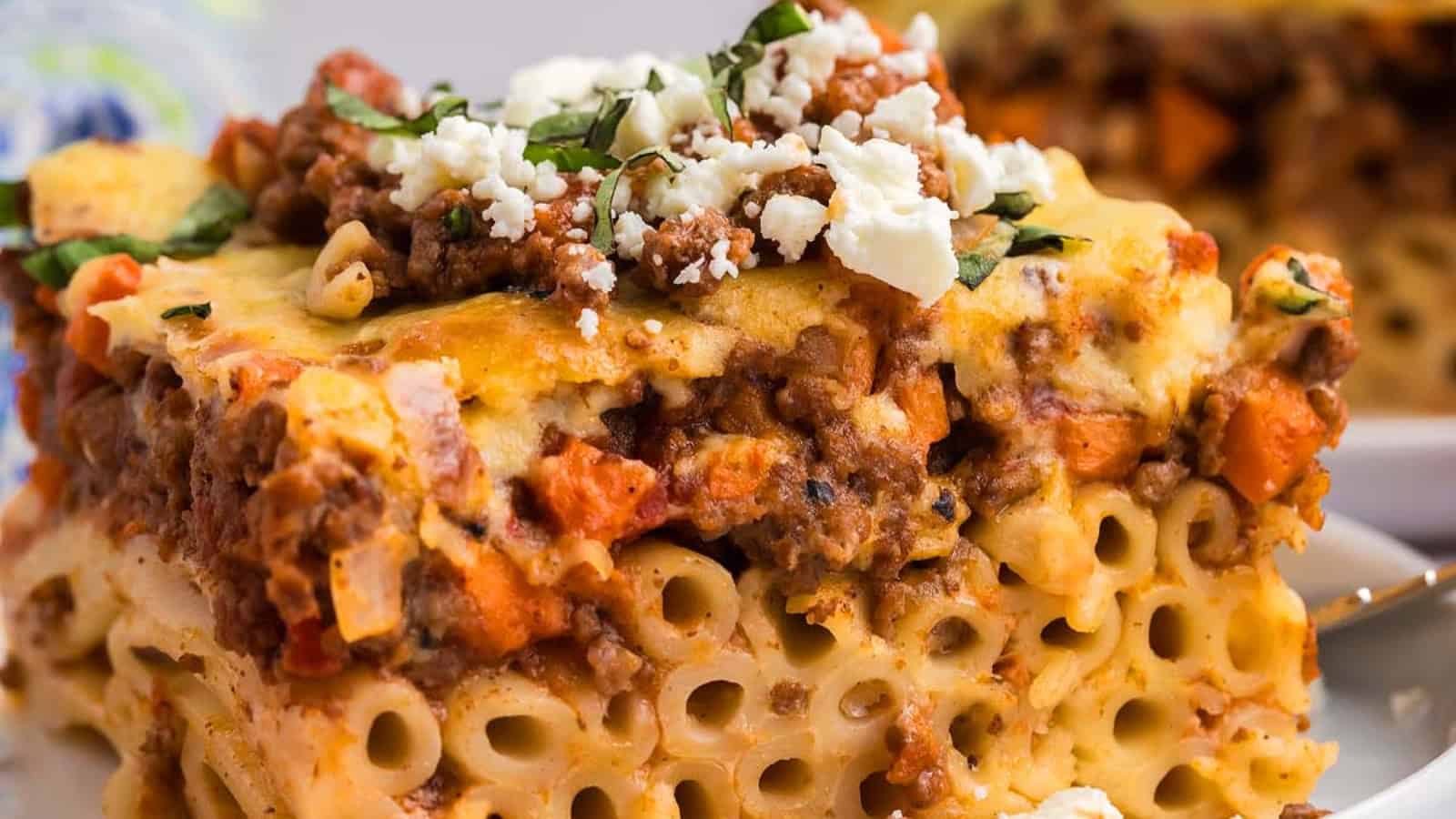 A close-up of a slice of baked pasta with meat sauce, topped with cheese and fresh herbs.