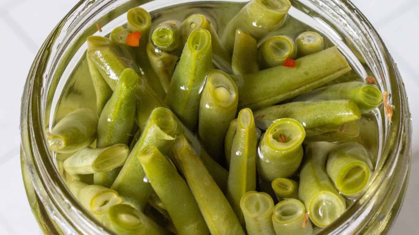 A jar filled with pickled green beans standing upright in clear brine.