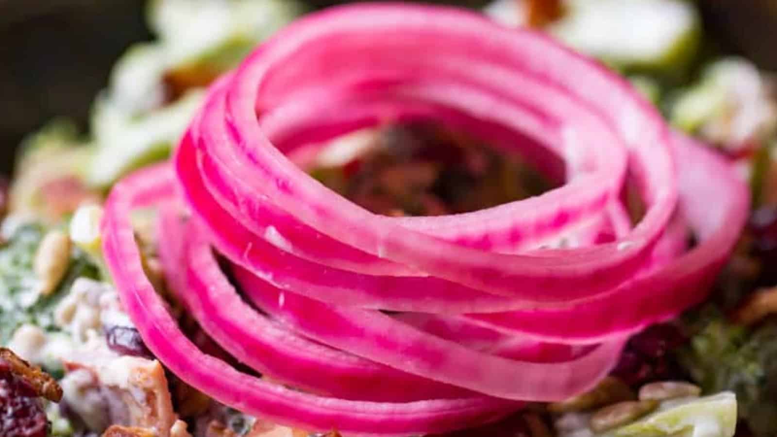 Thinly sliced pickled red onions arranged in a spiral on top of a colorful salad.