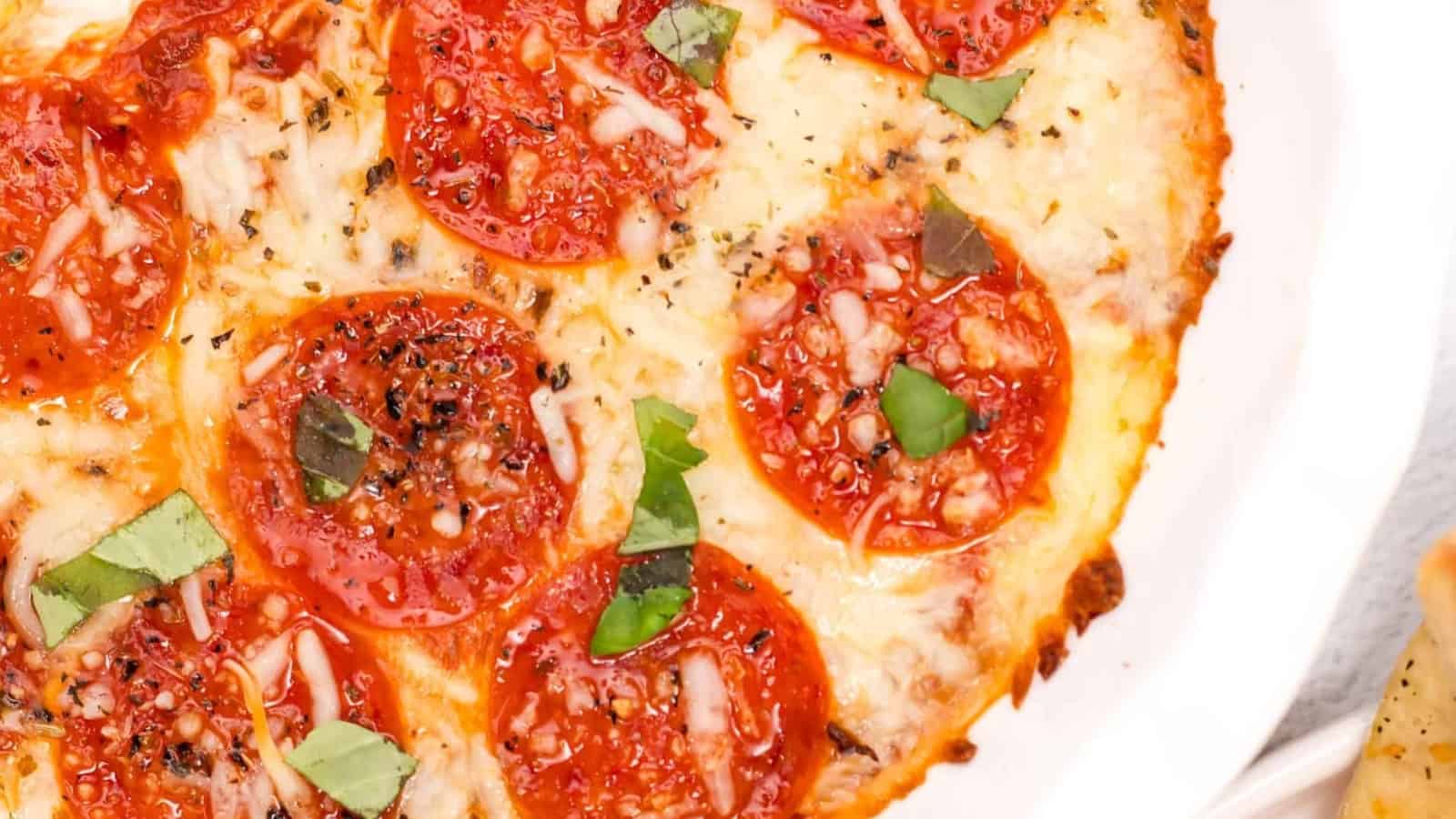 Close-up of a pepperoni pizza with melted cheese, fresh basil, and seasoning on a white plate.