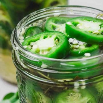 Sliced green jalapeños in a glass jar filled with brine, viewed from above.
