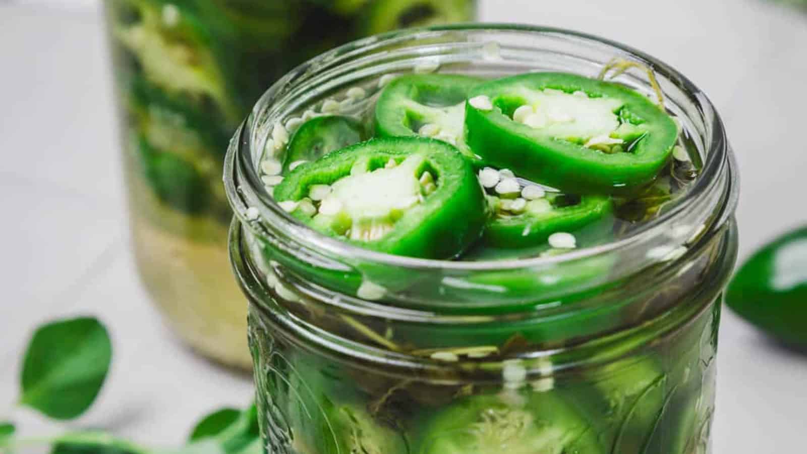 Sliced green jalape&ntilde;os in a glass jar filled with brine, viewed from above.