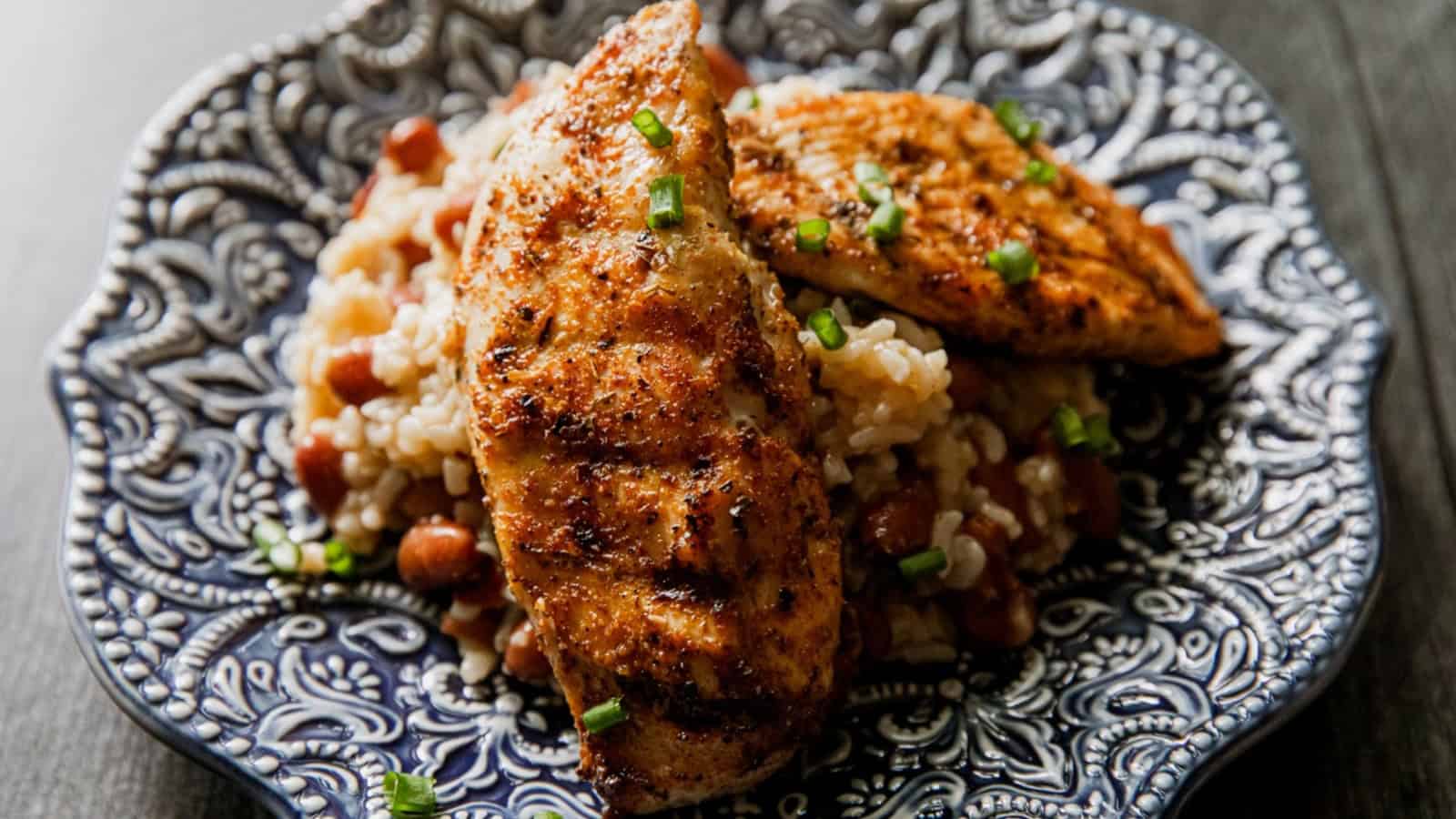 Grilled chicken breasts on rice and beans, garnished with chopped green onions on a patterned plate.
