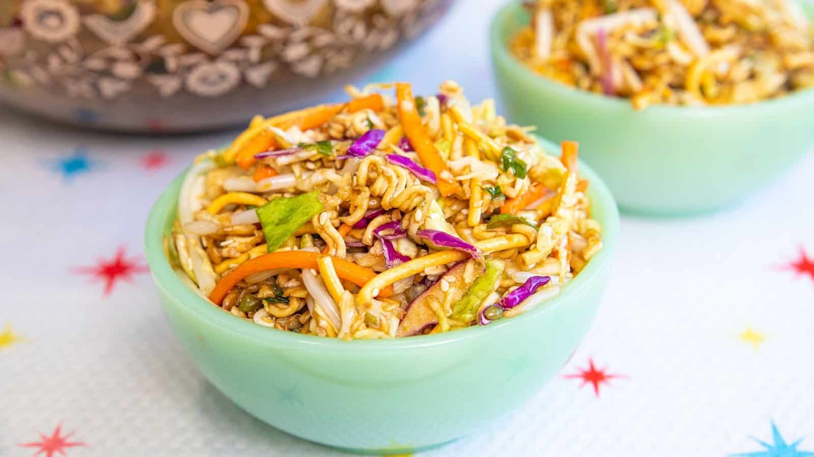 A green bowl filled with colorful Asian noodle salad, with cabbage, carrots, and crunchy noodles.