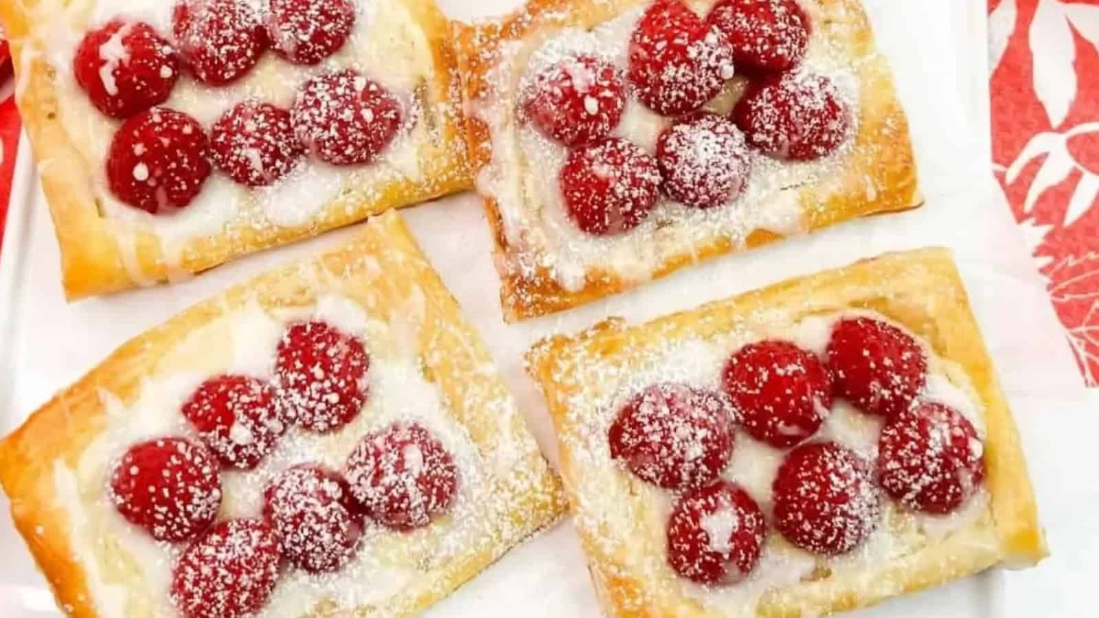 Four raspberry danishes with white icing and powdered sugar on a white plate.