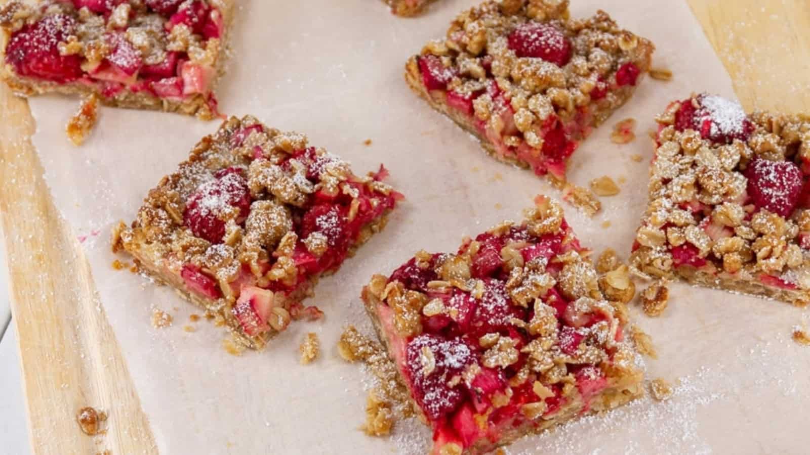 Six square fruit crumble bars with oats and powdered sugar on parchment paper.