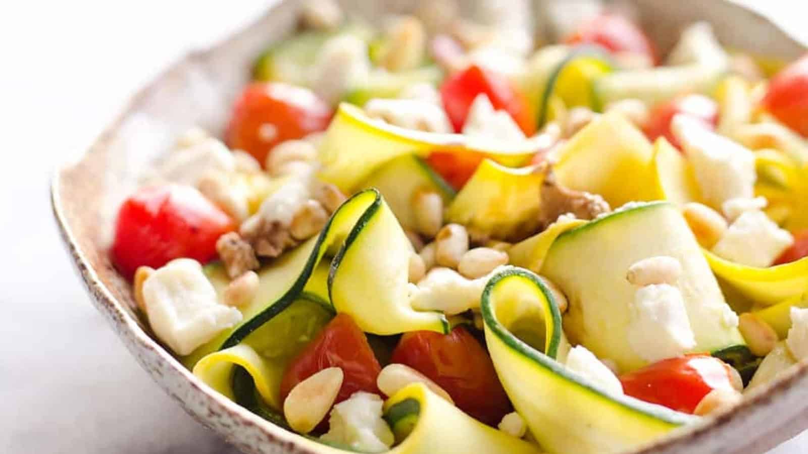 Zucchini ribbon salad with cherry tomatoes, feta cheese, pine nuts, and walnuts in a bowl.