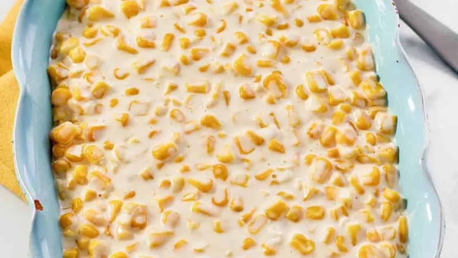 A baking dish filled with creamy corn casserole, with visible whole corn kernels in a thick sauce.
