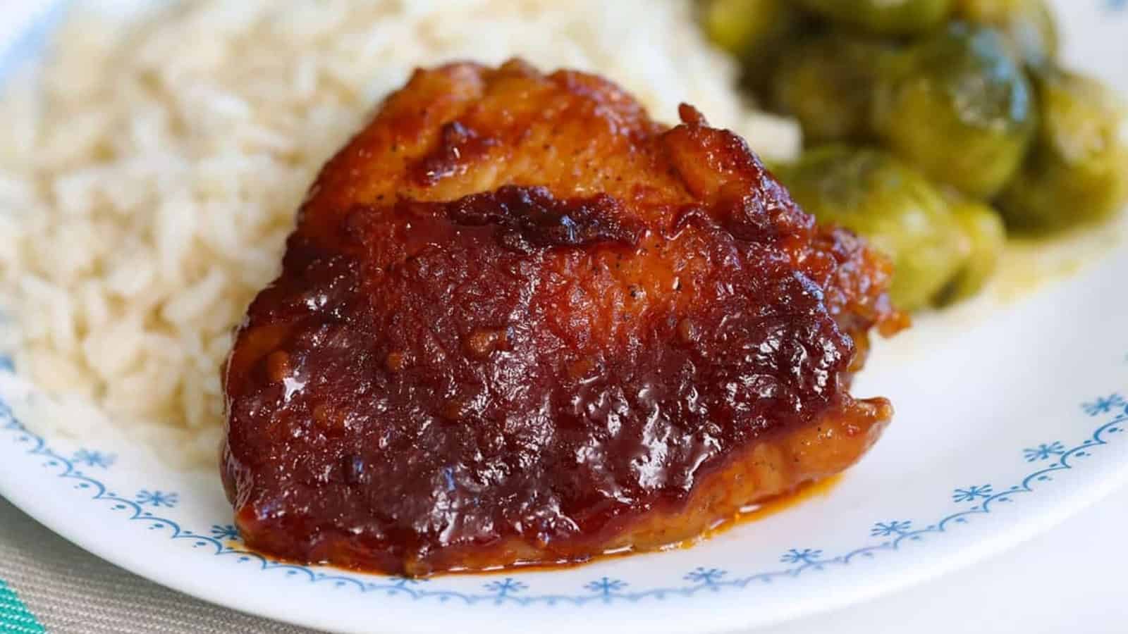 Barbecued chicken thigh with white rice and Brussels sprouts on a white plate.