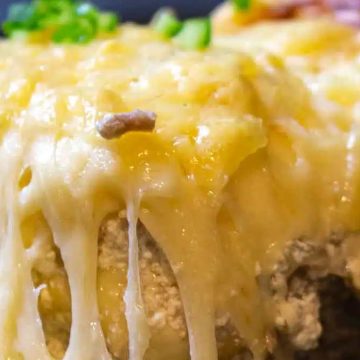 Close-up of melted cheese oozing over a baked casserole with ground meat and toppings.