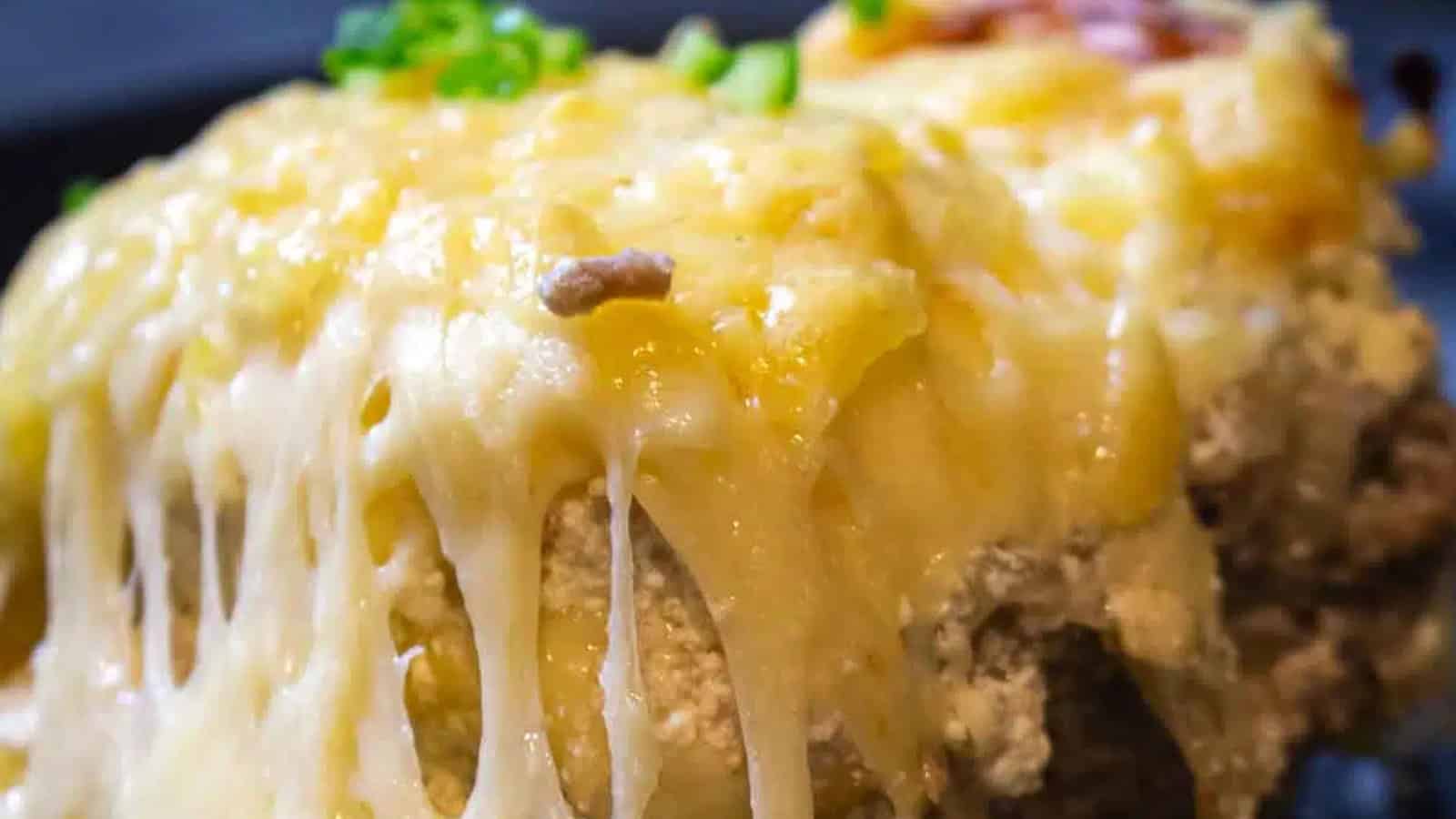 Close-up of melted cheese oozing over a baked casserole with ground meat and toppings.