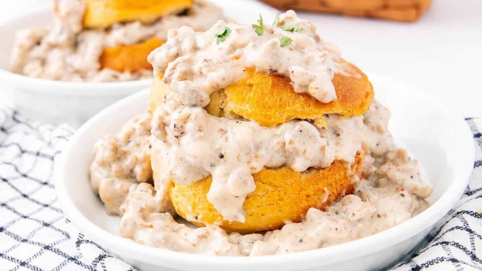 Biscuits topped with creamy sausage gravy on a white plate, with a checkered napkin underneath.