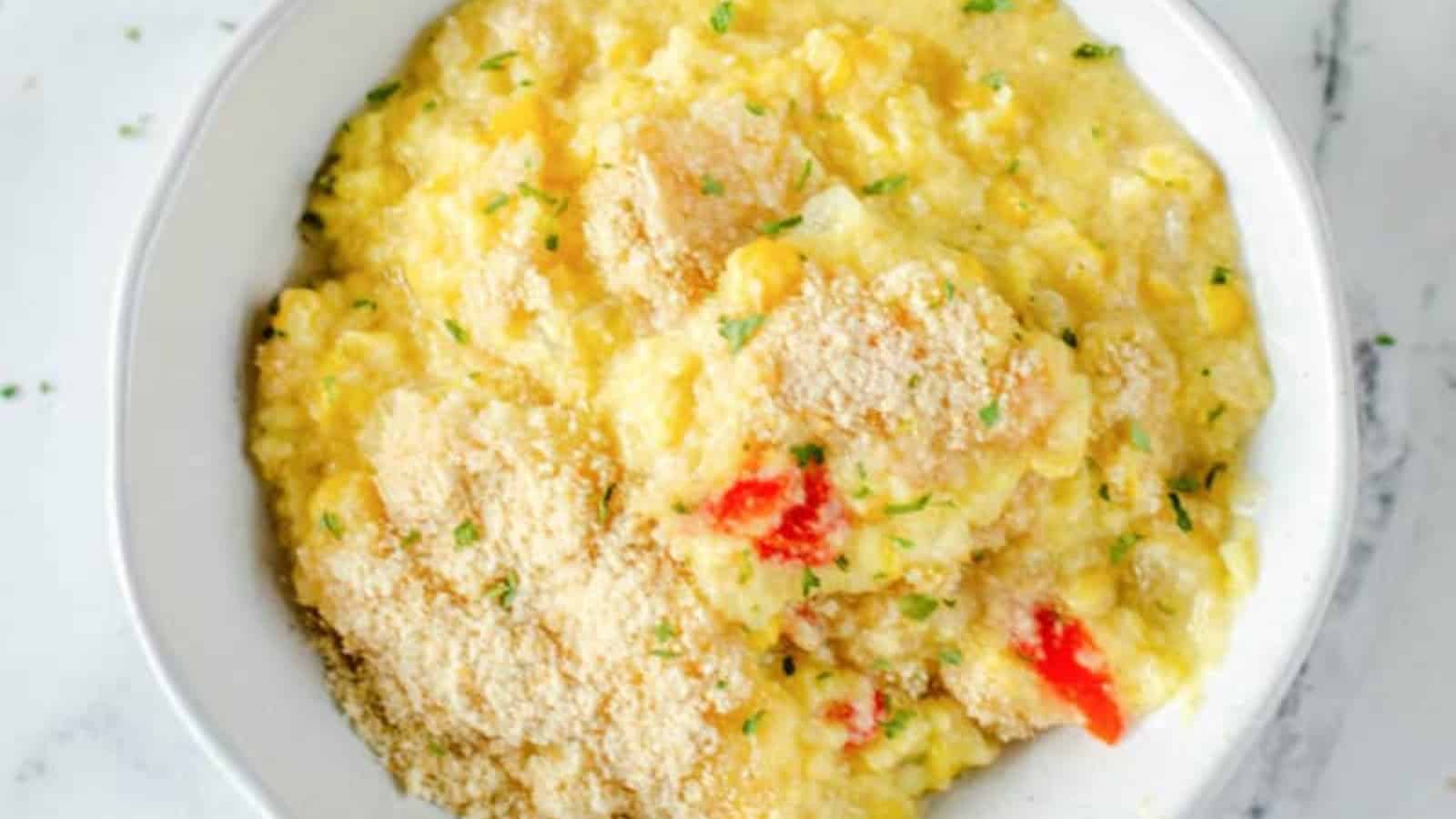 Bowl of cheesy corn casserole topped with breadcrumbs and garnished with chopped parsley.