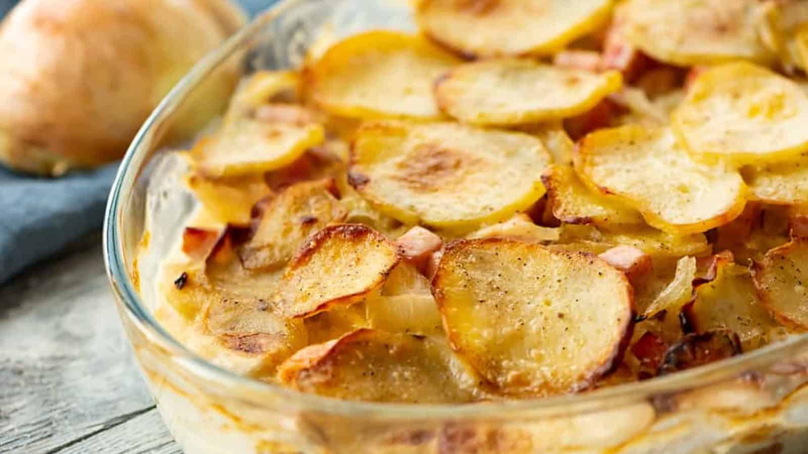 A close-up of a baked potato gratin in a glass dish, with golden, crispy potato slices on top.