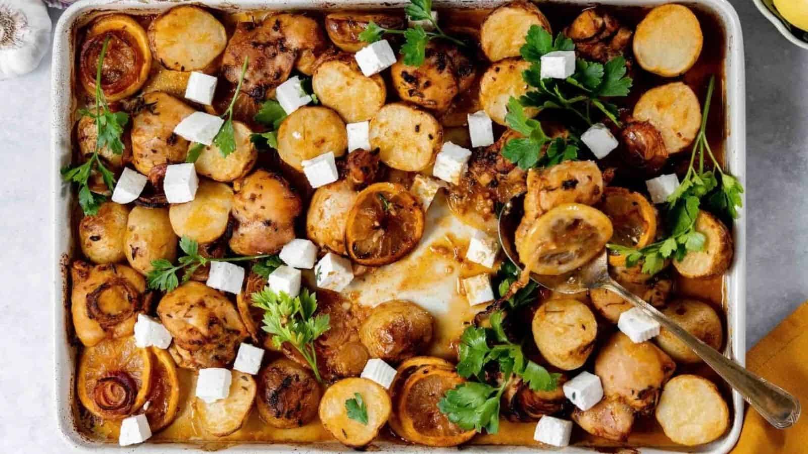 Baked chicken and potatoes with herbs, garnished with fresh parsley and cubes of white cheese on a tray.