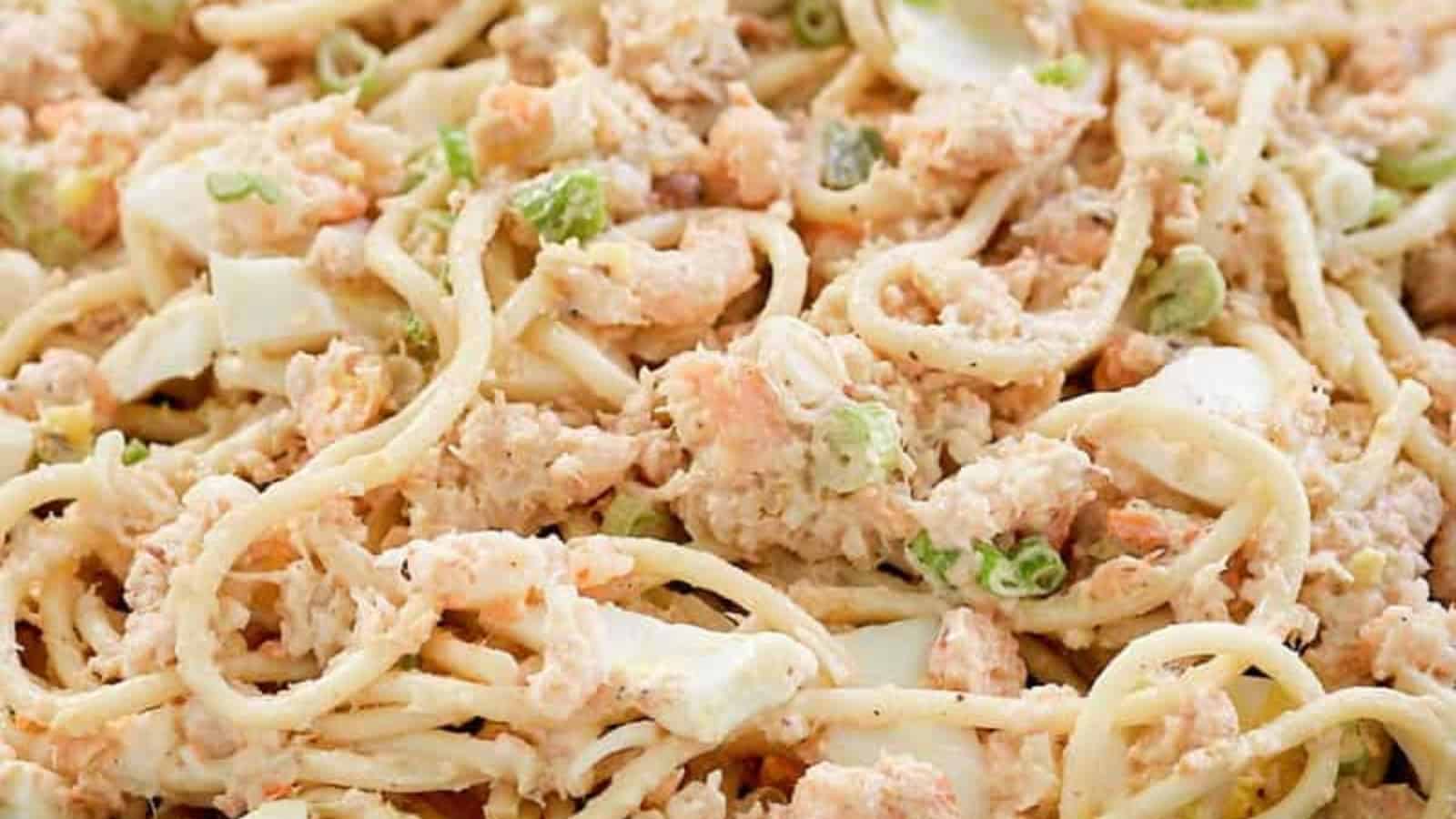 Close-up of creamy tuna pasta salad with noodles, chopped eggs, and green onions.