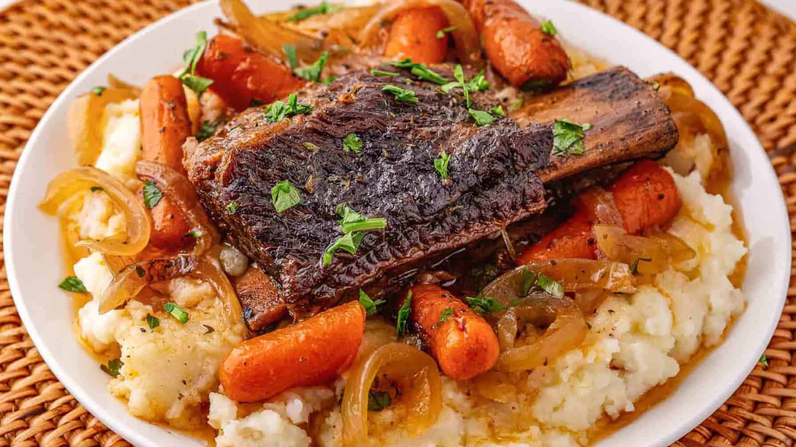 Braised short rib with carrots and onions served over mashed potatoes, garnished with chopped parsley.