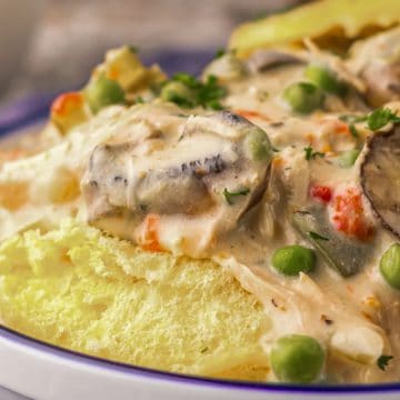 Creamy chicken à la king with mushrooms, peas, and carrots served over a fluffy biscuit on a plate.