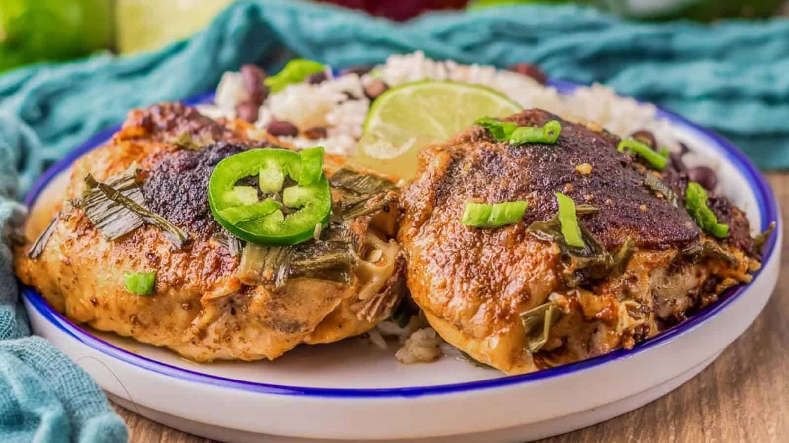 A plate with two pieces of seasoned baked chicken garnished with sliced jalape&ntilde;os, served on a bed of rice with beans and a lime wedge.