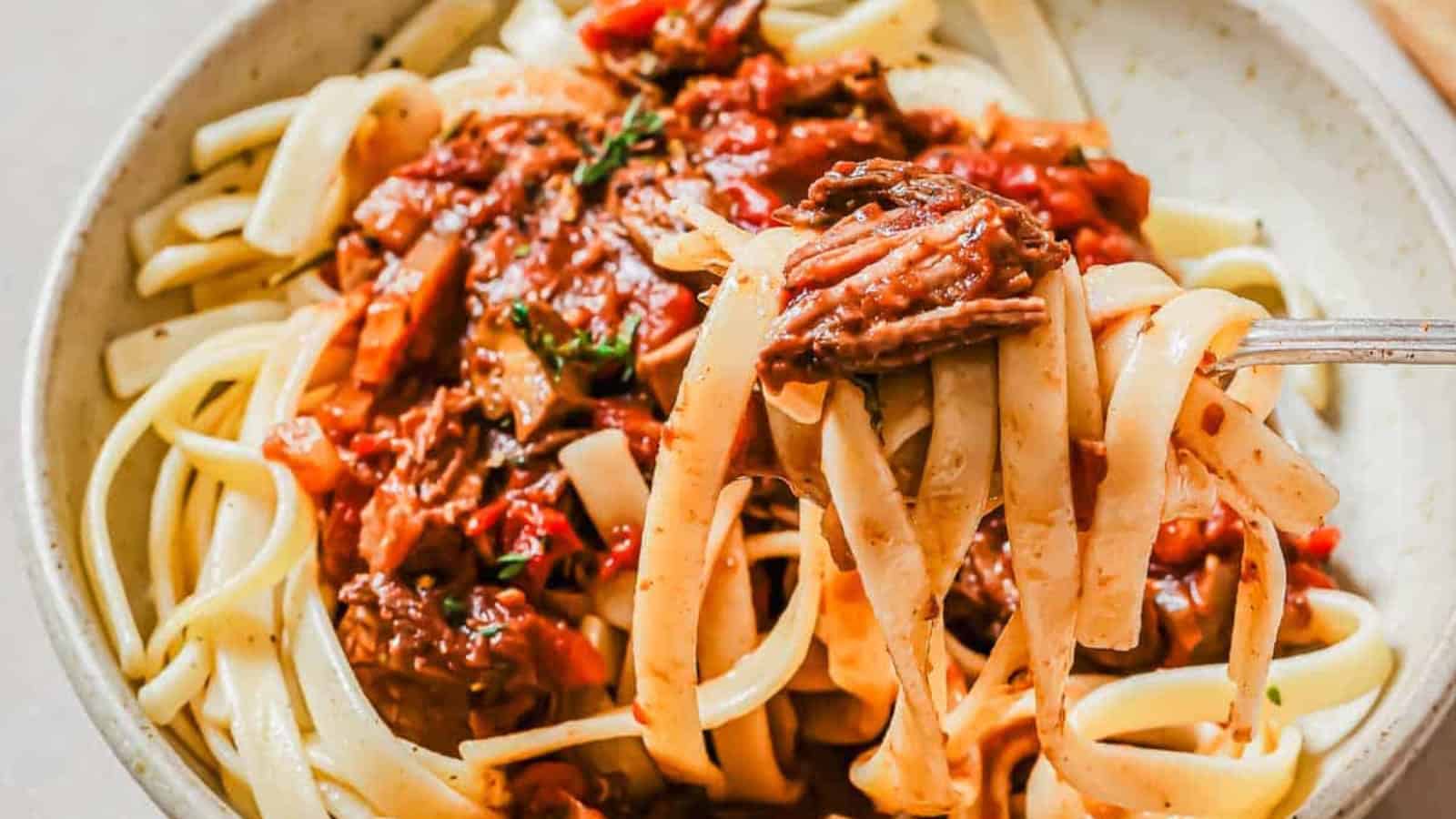 Slow cooker short rib ragu in a bowl over mashed sweet potatoes with a fork.