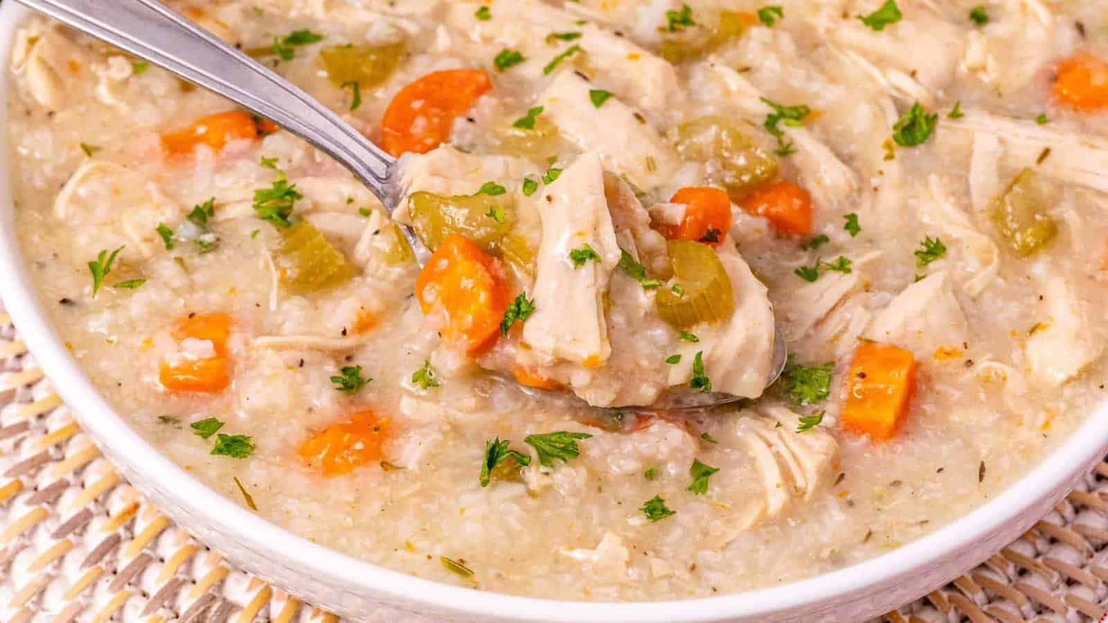 Bowl of chicken and rice soup with carrots, celery, and herbs, with a spoon scooping some up.