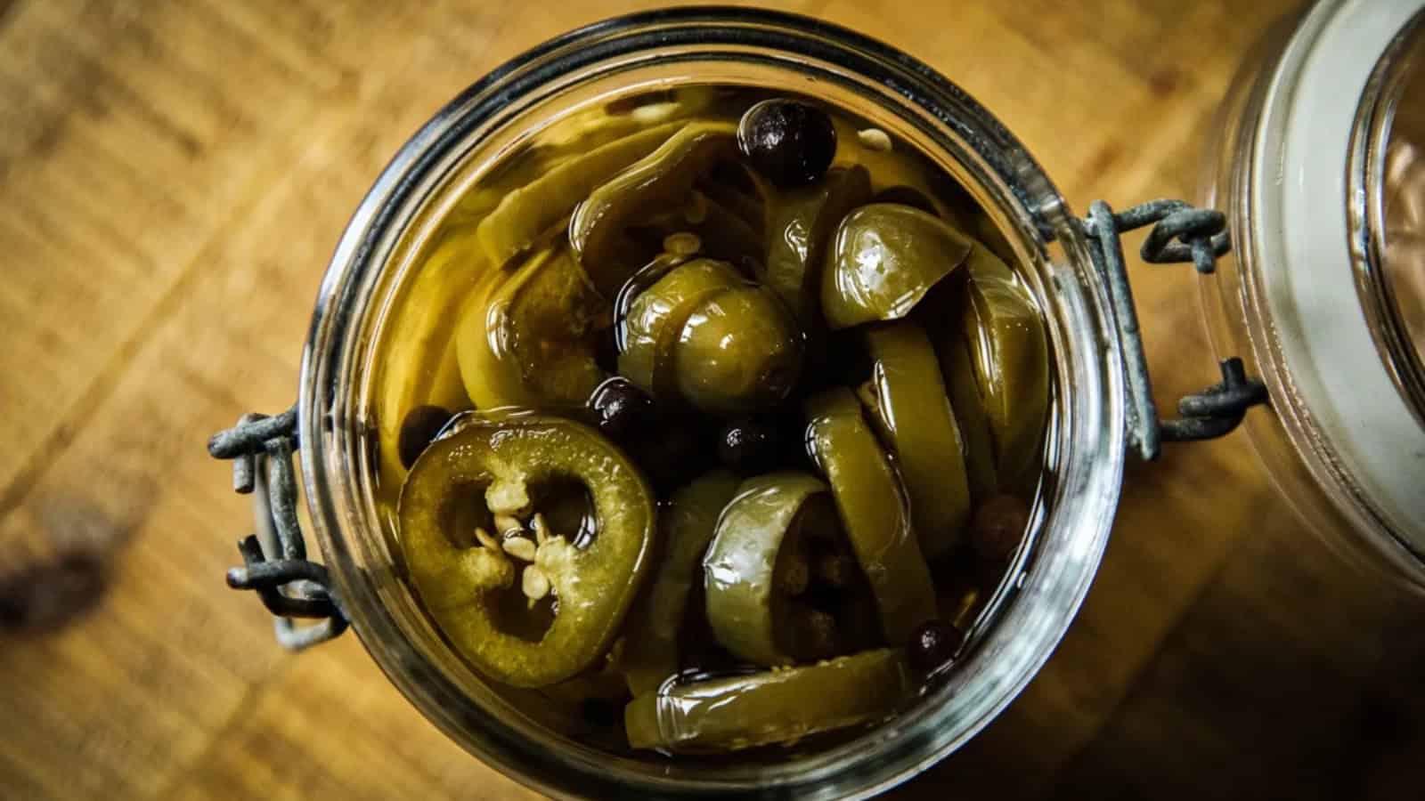 A glass jar filled with sliced pickled jalapeños and spices, viewed from above on a wooden surface.