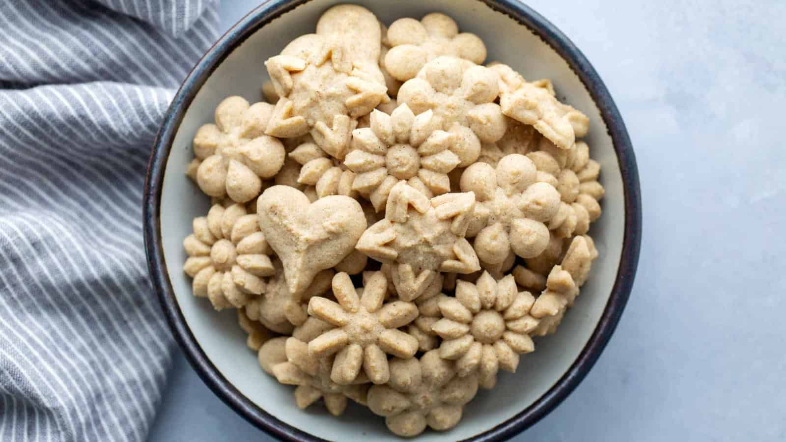 A bowl filled with assorted, flower-shaped and heart-shaped cookies beside a striped cloth.