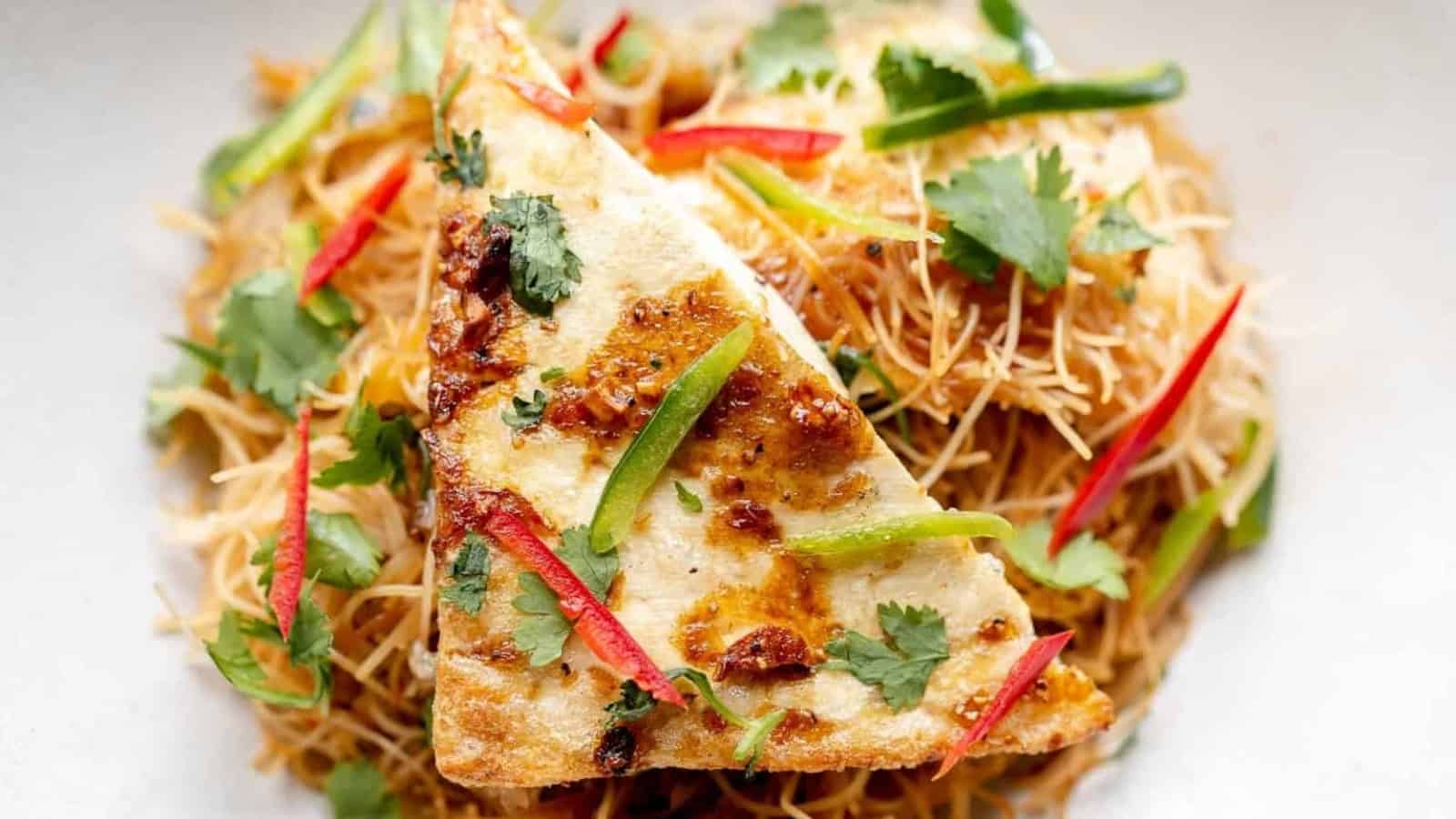 Fried tofu on stir-fried noodles, garnished with cilantro and red and green pepper strips.