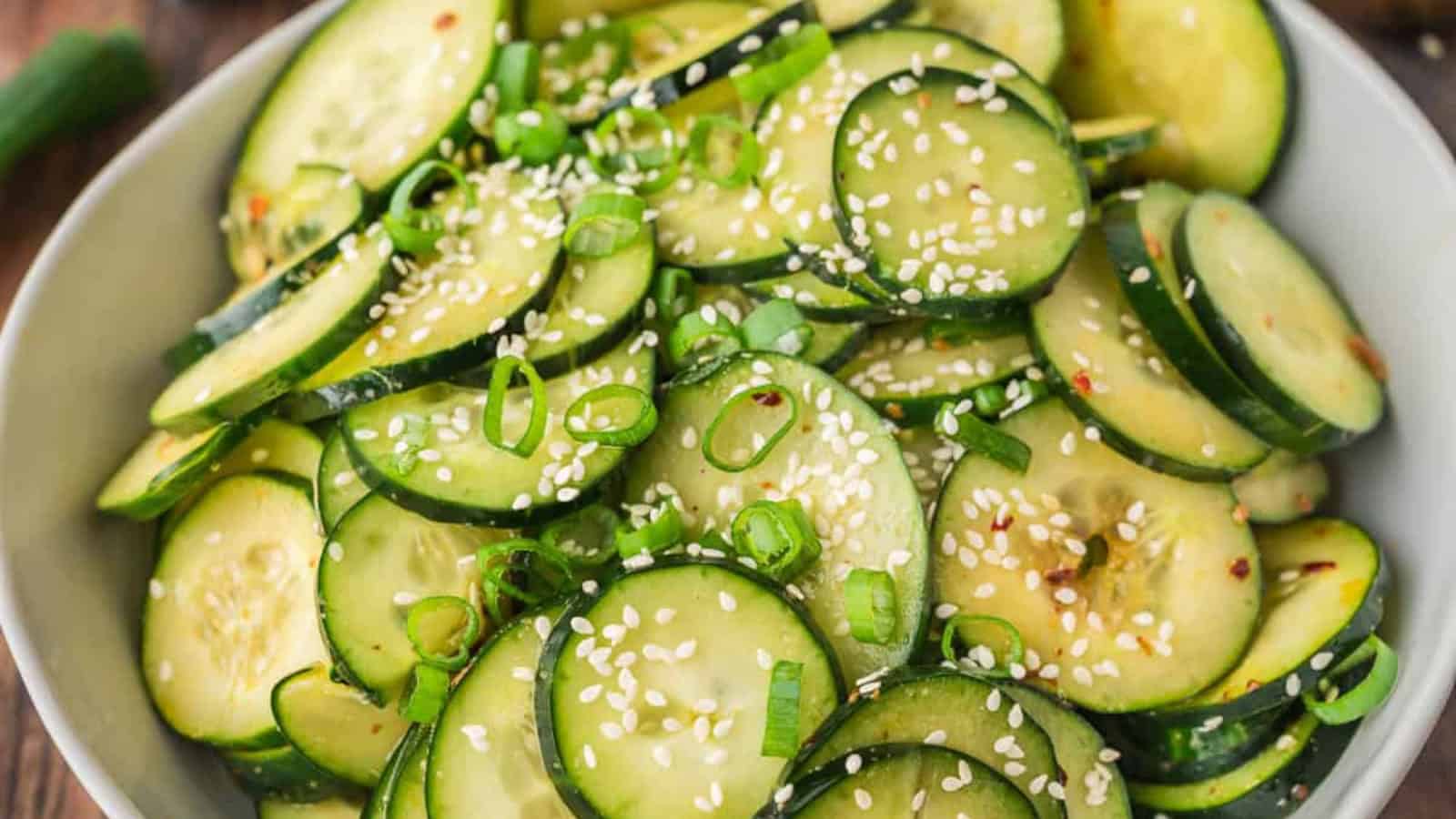 Sliced cucumber salad topped with sesame seeds and chopped green onions in a white bowl.