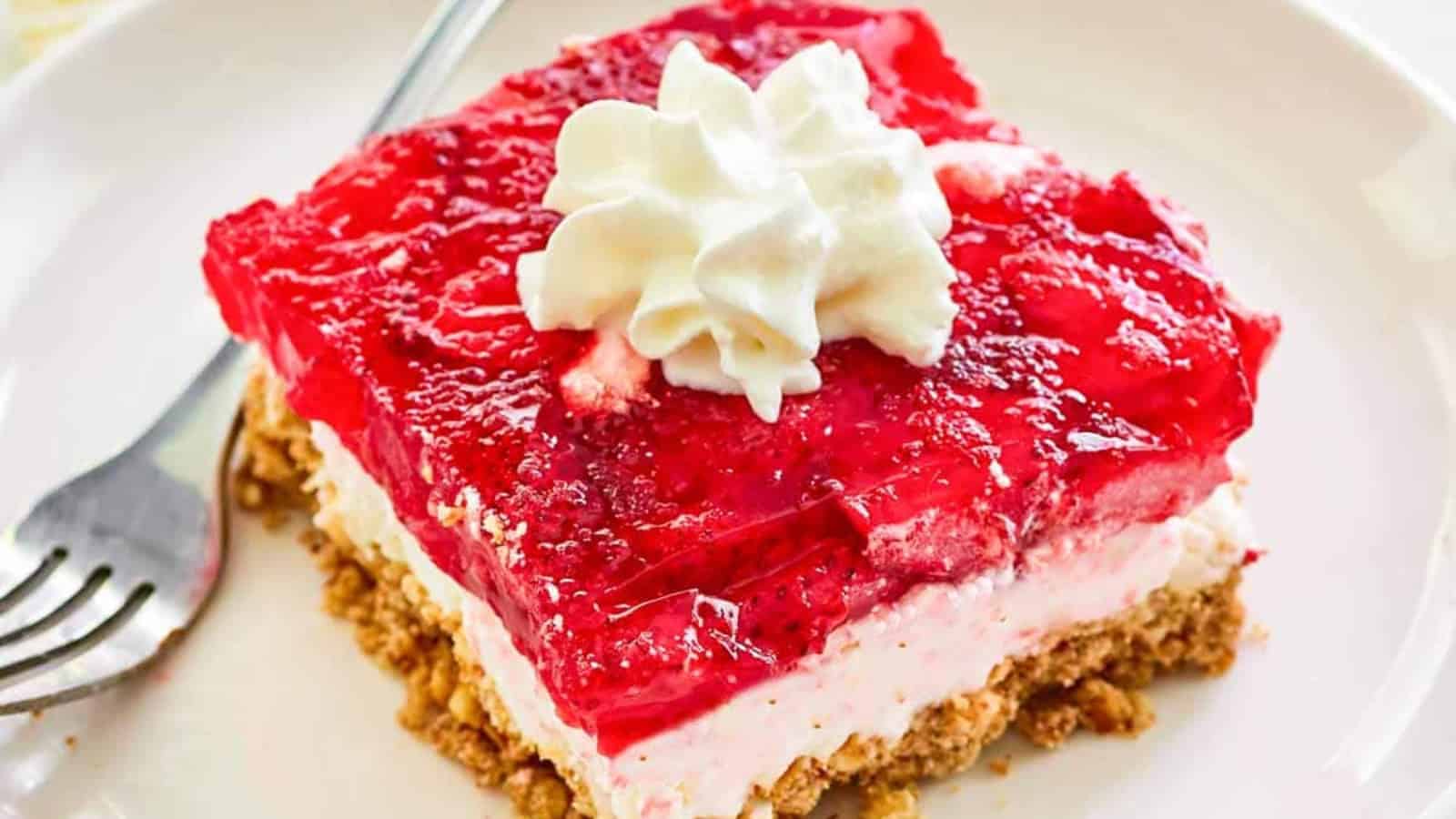 A slice of strawberry pretzel salad topped with whipped cream sits on a plate with a fork.