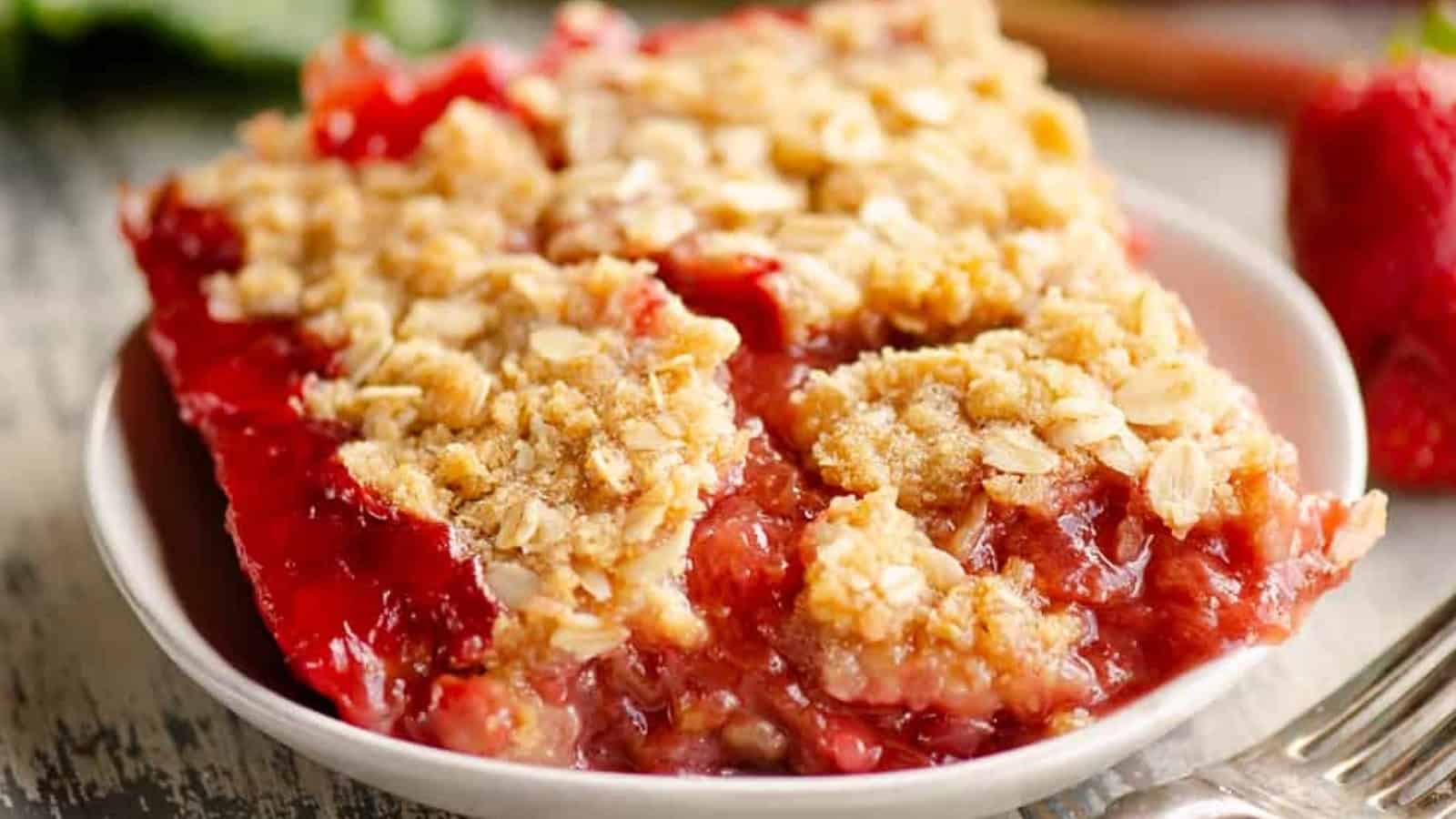 A slice of strawberry crumble dessert with oat topping on a white plate.
