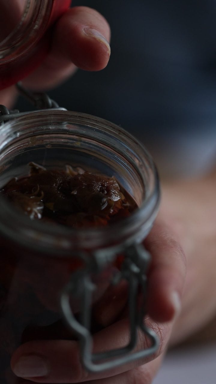 A hand opening a glass jar filled with what appears to be preserved food in liquid.